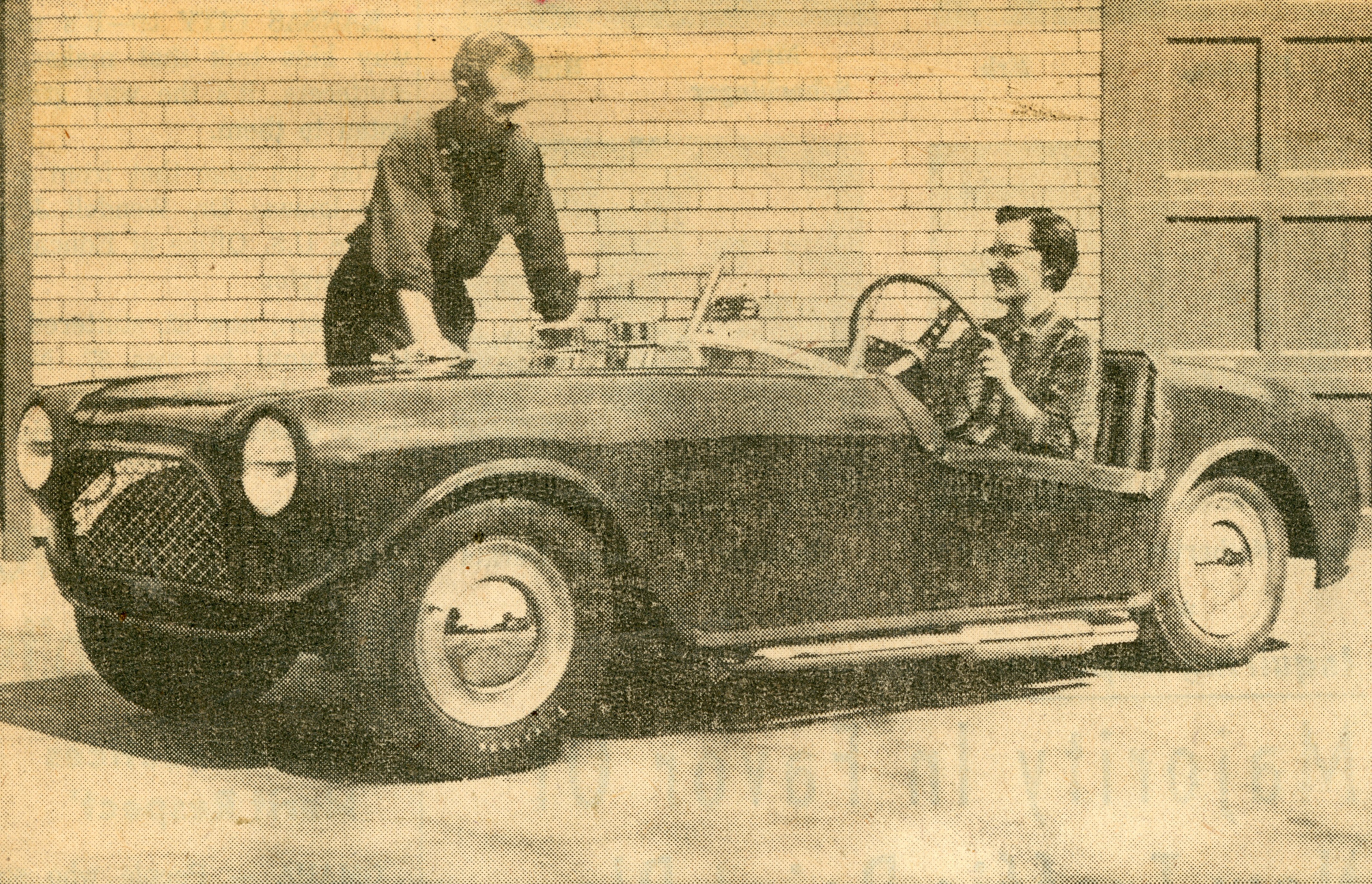 Photo of Alfred Clemens standing by his custom-built car with his wife in the driver's seat