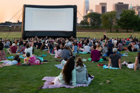 Photo of an outdoor movie screen with audience viewing from the grass.