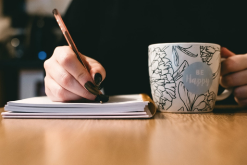 Unidentified hand writing on pad with coffee mug