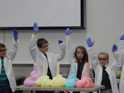 Children with their hands in the air and floam on the table.